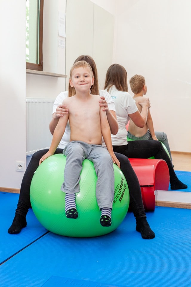 fizjoterapeuta i chłopczyk siedzą na piłce gimnastycznej podczas rehabilitacji
