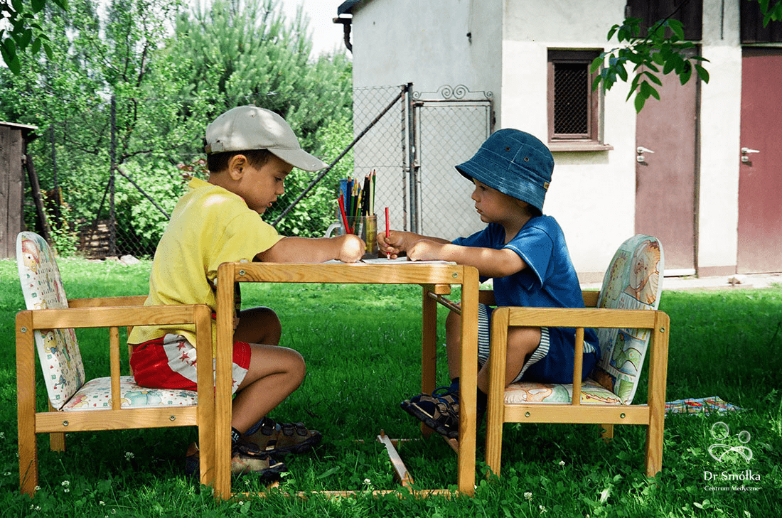 chłopcy siedzący przy stoliku w ogrodzie rysujący kredkami