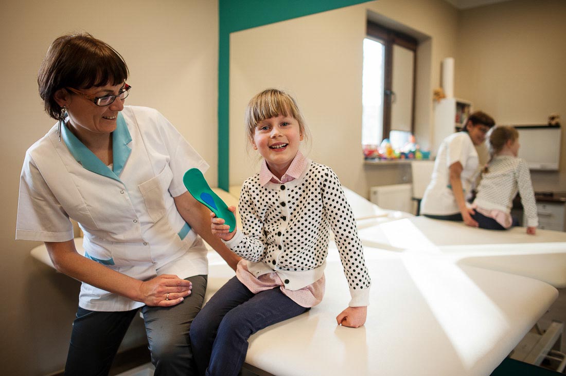uśmiechnięta dziewczynka siedząca obok lekarza trzymająca w ręce wkładkę ortopedyczną