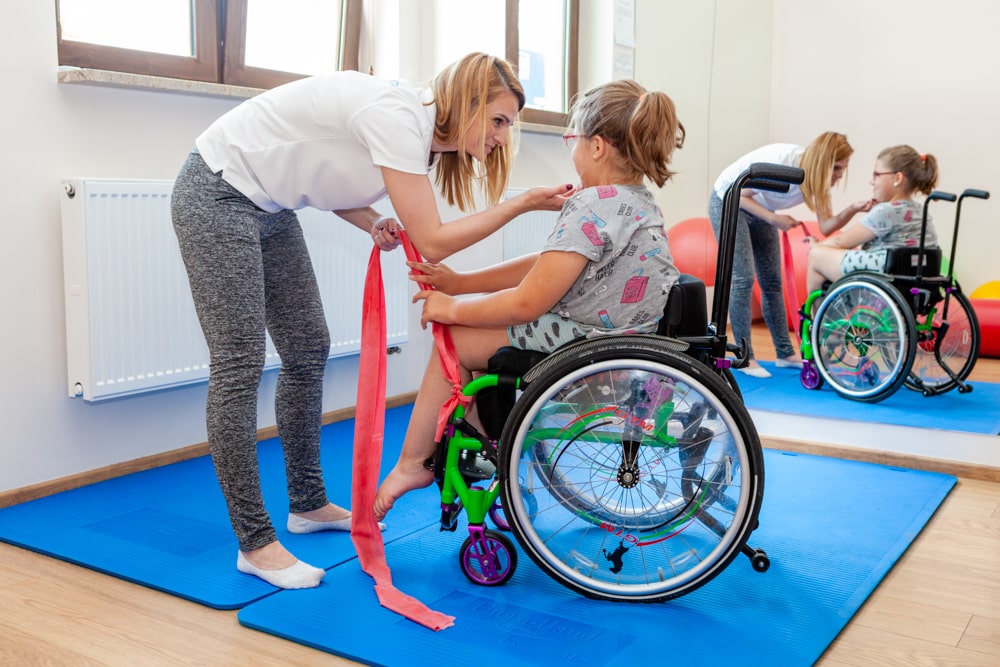 dziewczynka na wózku inwalidzkim podczas rehabilitacji z fizjoterapeutą