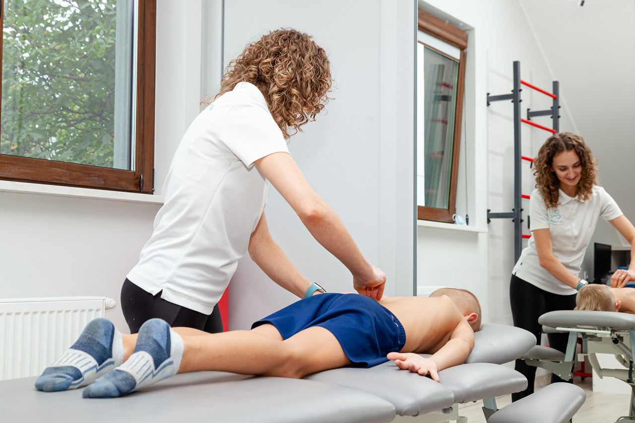 fizjoterapeuta podczas rehabilitacji skoliozy u dziecka na łóżku fizjoterapeutycznym