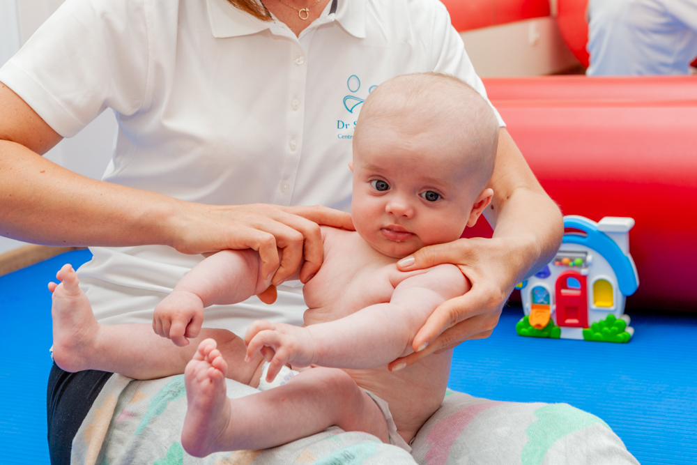 fizjoterapeuta trzyma niemowlę na kolanach podczas terapii neurorozwojowej